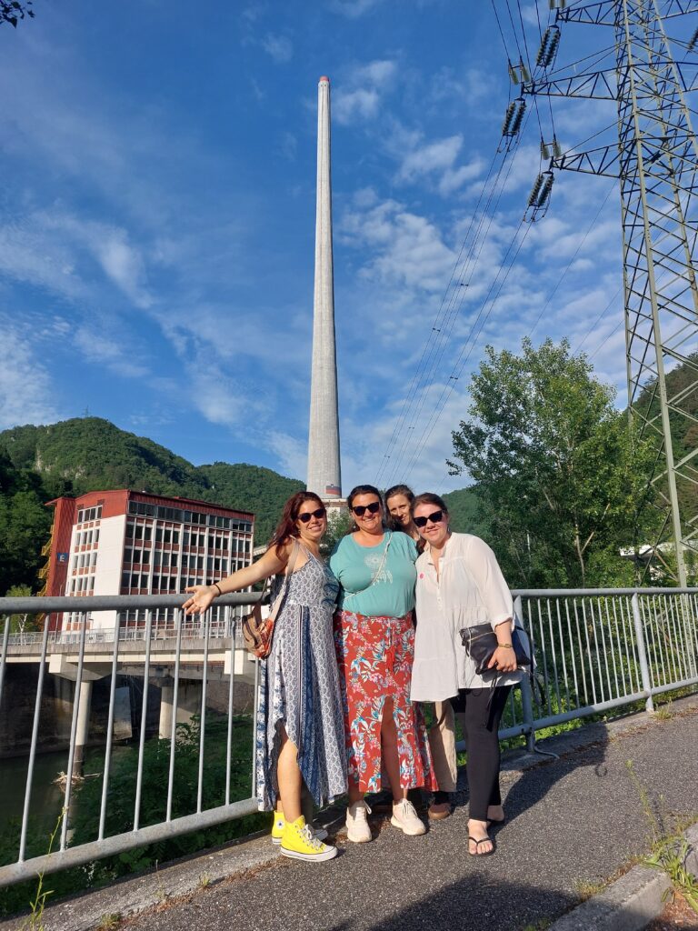 Udeleženke projekta pred industrijskim objektom z dimnikom.